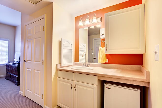 A modern bathroom with a sink, mirror, and cabinetry against an orange accent wall.