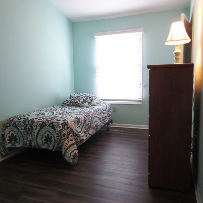 A minimalist bedroom with a single bed, dresser, and a lamp by the window.