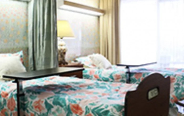 A hospital room featuring two beds with floral bedspreads and a bedside lamp.