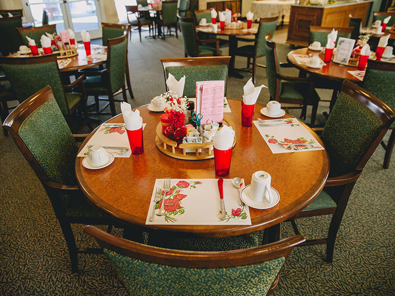 A warmly set dining table with placemats, red cups, and arranged napkins in a restaurant setting.