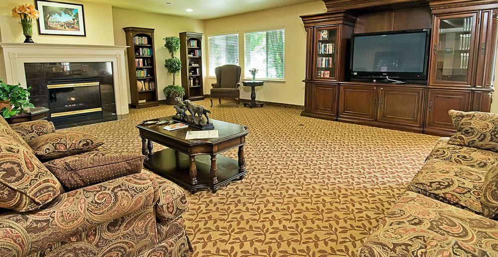 A spacious living room with elegant furniture, featuring bookshelves, a TV stand, and a patterned carpet.