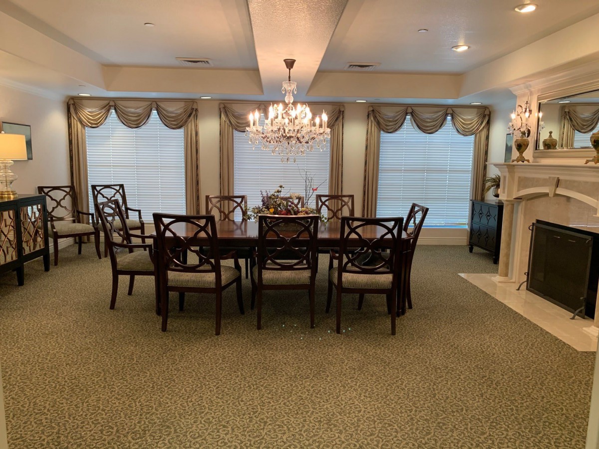 A spacious dining room featuring a large table with multiple chairs, elegant chandeliers, and decorative curtains.