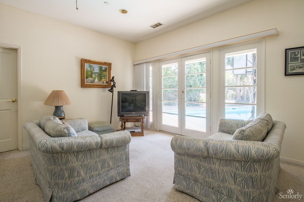 A cozy living room with sofas, a TV, large windows, and a view of the pool.
