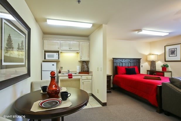 A compact studio apartment featuring a kitchenette and a cozy bedroom with red bedding.