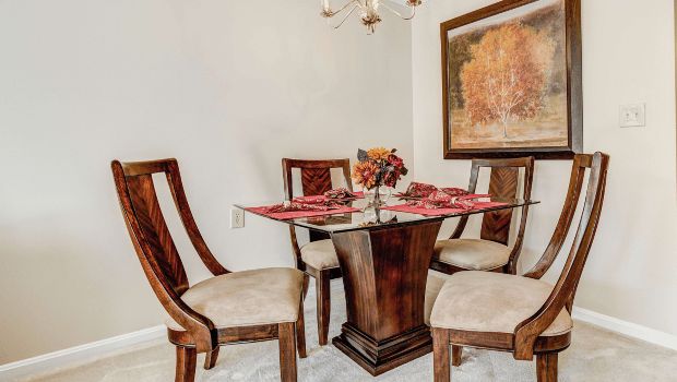 A stylish dining room with a glass-top table and four wooden chairs, adorned with elegant decor and artwork.