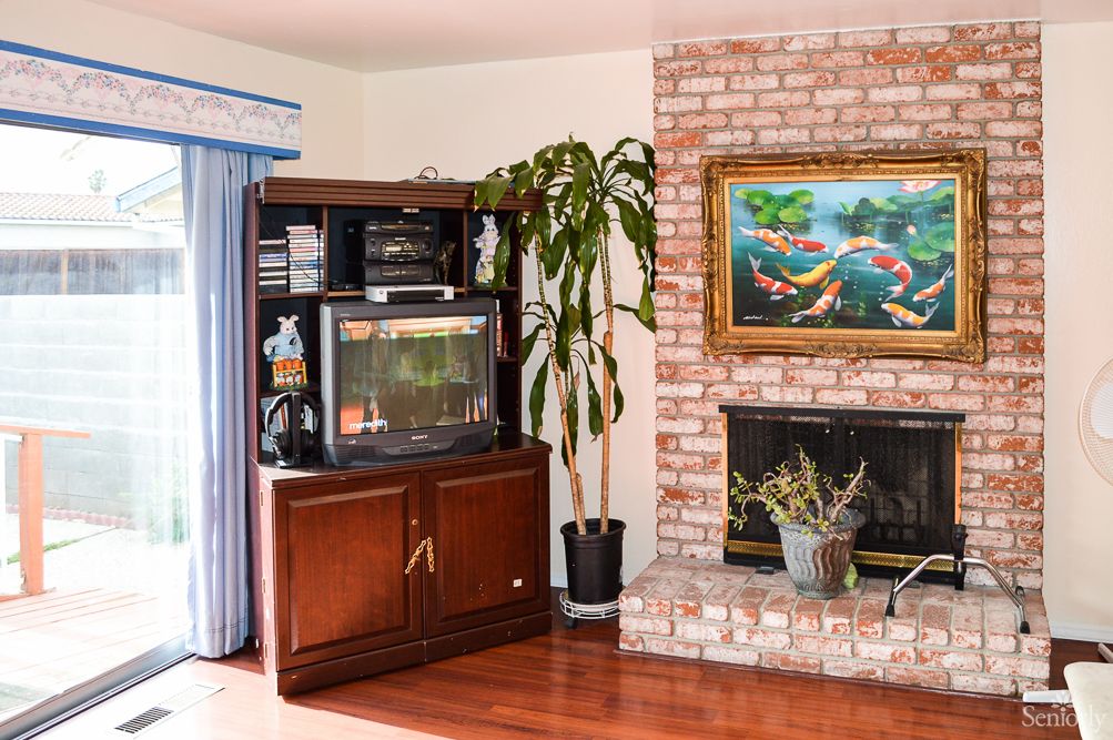 A cozy living room featuring a brick fireplace, an entertainment center with an aquarium, a potted plant, and a colorful painting on the wall.