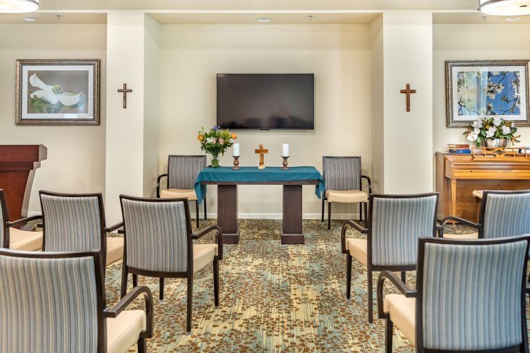 A small chapel interior with an altar, chairs arranged for a congregation, and religious symbols on the walls.