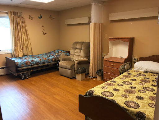 A spacious and comfortable shared room in a senior living facility, featuring beds, chairs, and warm decor.