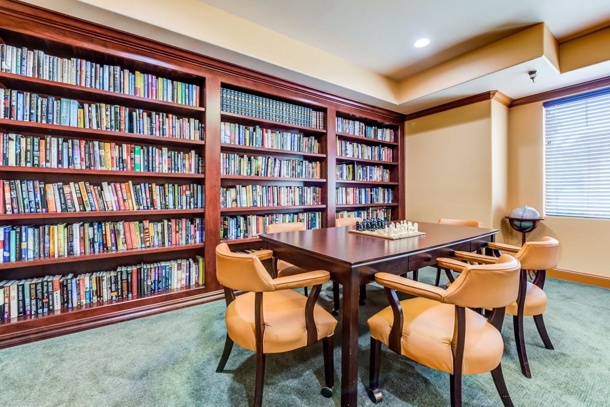 A cozy library room with wooden bookshelves filled with books, surrounding a central table and chairs, ideal for reading or meetings.