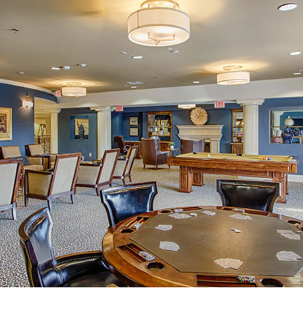 A spacious recreational room featuring a poker table and a pool table, surrounded by comfortable seating and elegant lighting.