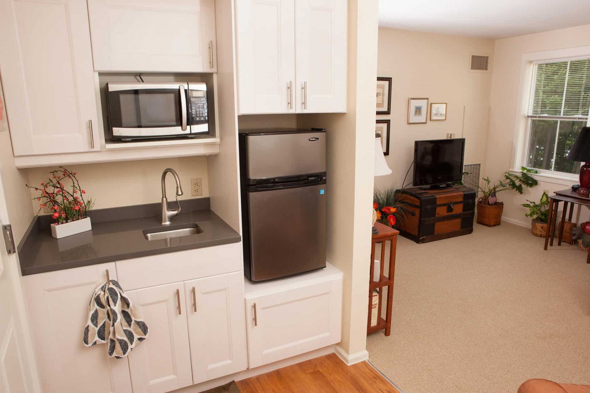 A compact kitchenette with a microwave, refrigerator, and sink adjacent to a cozy living room.