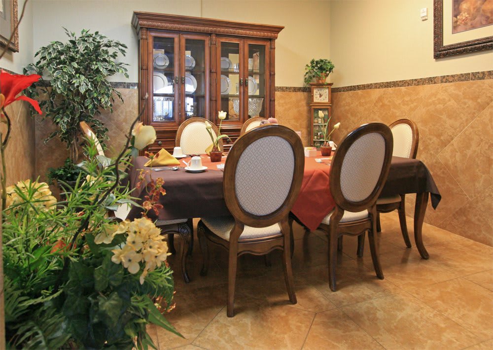 An elegant dining room setup with a wooden table, cushioned chairs, and a china cabinet, adorned with indoor plants.
