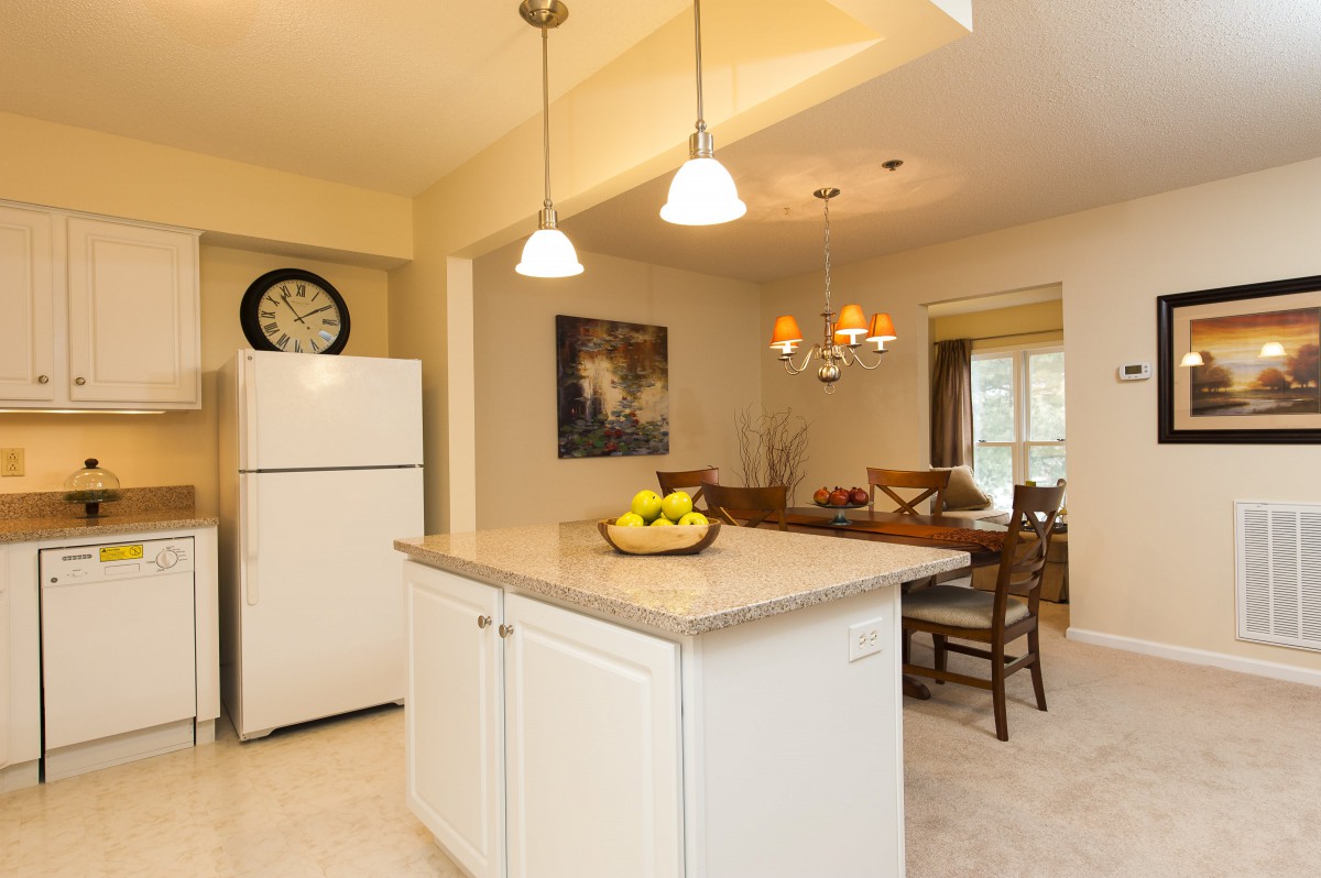 A cozy kitchen and dining area featuring an island counter with pendant lights, a refrigerator, and a chandelier over the dining table.