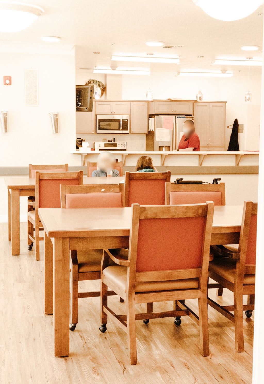 A cozy dining area with wooden tables and chairs, adjacent to a kitchen.