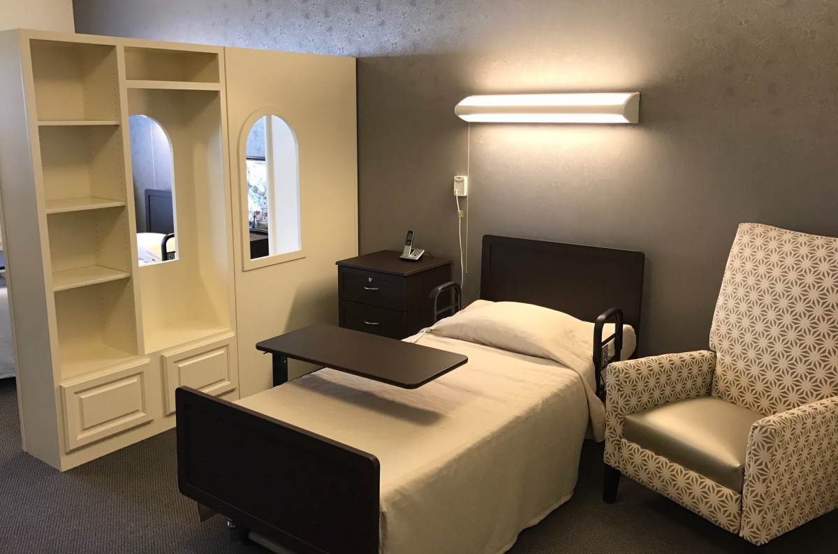 A hospital room featuring a bed, side table, and chair under soft lighting.