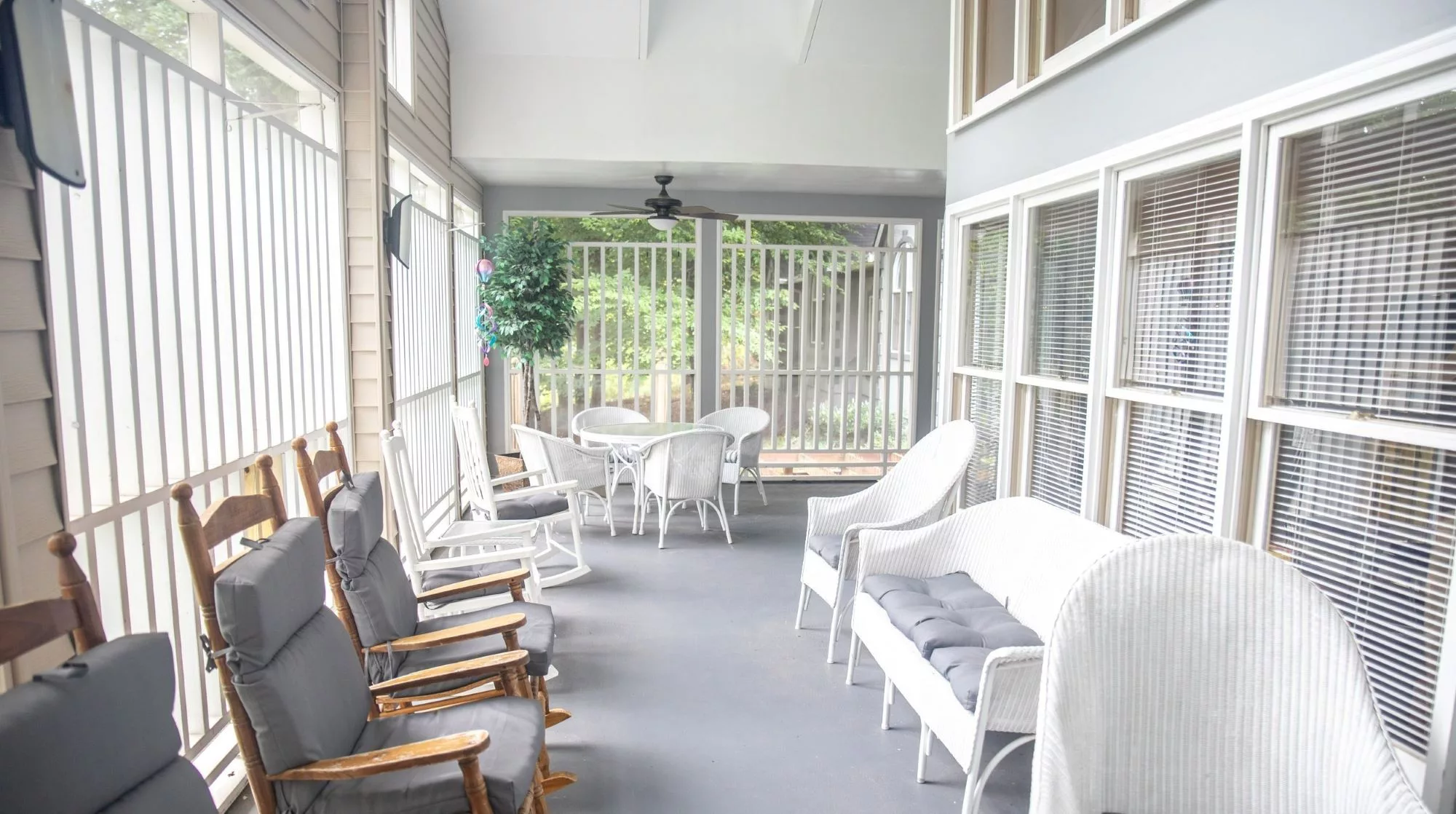 A cozy enclosed porch with comfortable seating, including wicker furniture and rocking chairs, offering a bright and relaxing atmosphere.