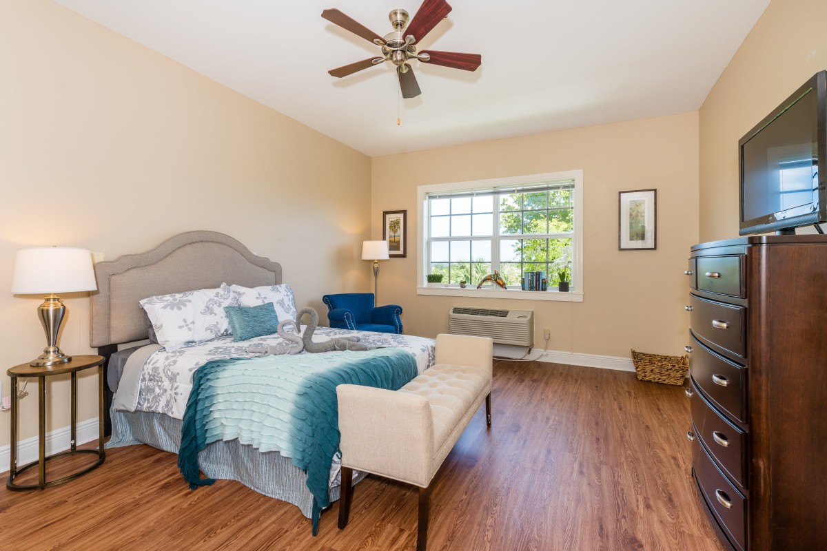 A cozy bedroom with a bed, armchair, and large window allowing natural light.