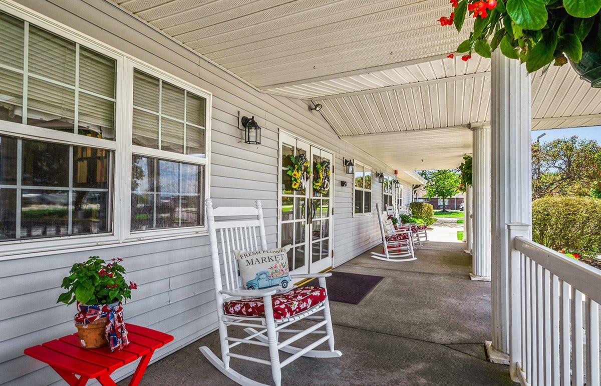 A cozy porch with white rocking chairs and colorful cushions, adorned with hanging flowers.