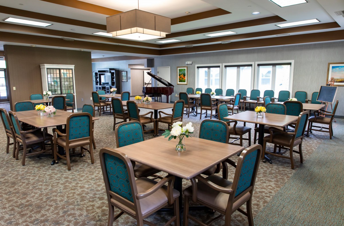 A spacious dining area with neatly arranged tables and chairs, featuring a piano in the background.