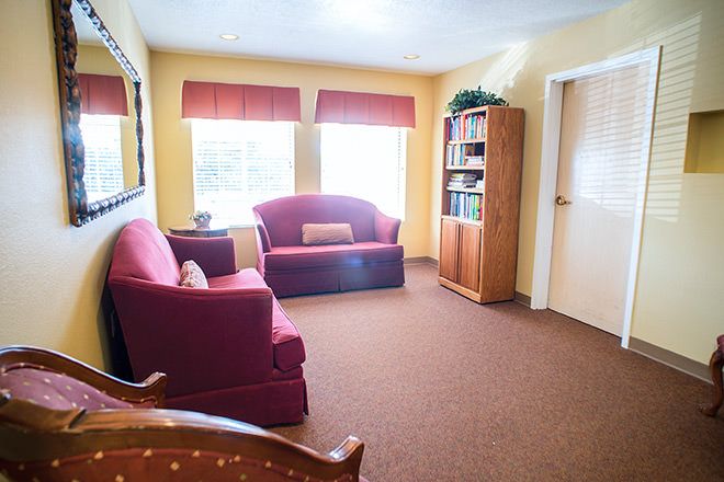 A cozy living room with red sofas, a bookshelf, and large windows.