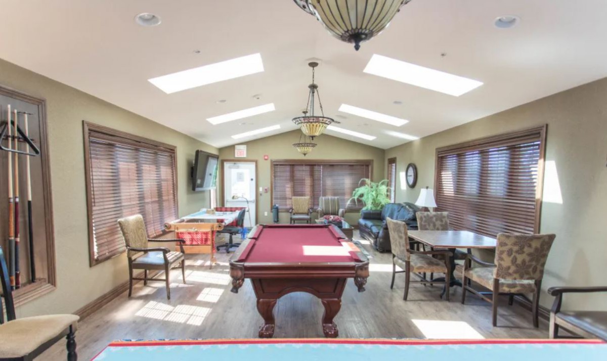 A well-lit recreation room featuring a pool table, seating area, and large windows.