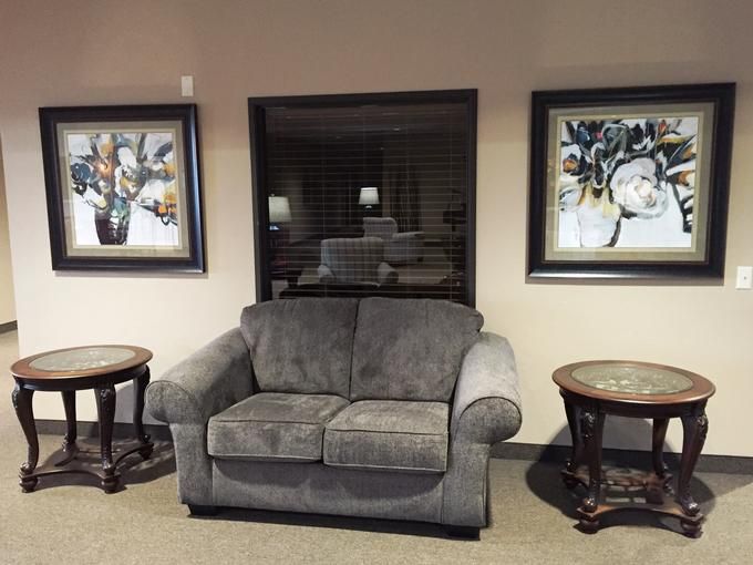 A cozy living room setup with a plush gray loveseat, flanked by round wooden coffee tables and complemented by framed artwork on the wall.