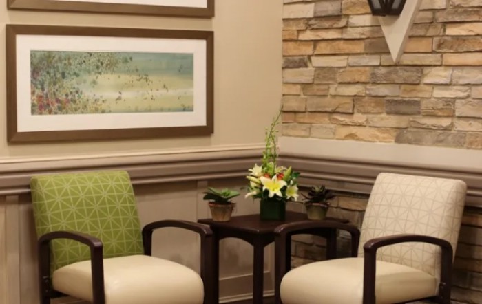 A cozy waiting room with two chairs and a table adorned with a flower arrangement, framed artwork, and a stone accent wall.