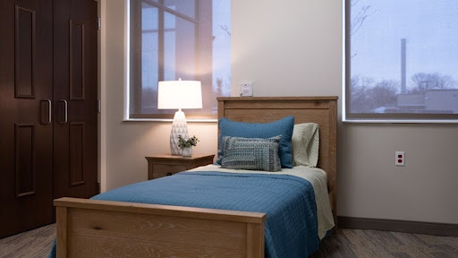 A cozy bedroom featuring a single wooden bed with blue bedding and a lamp.