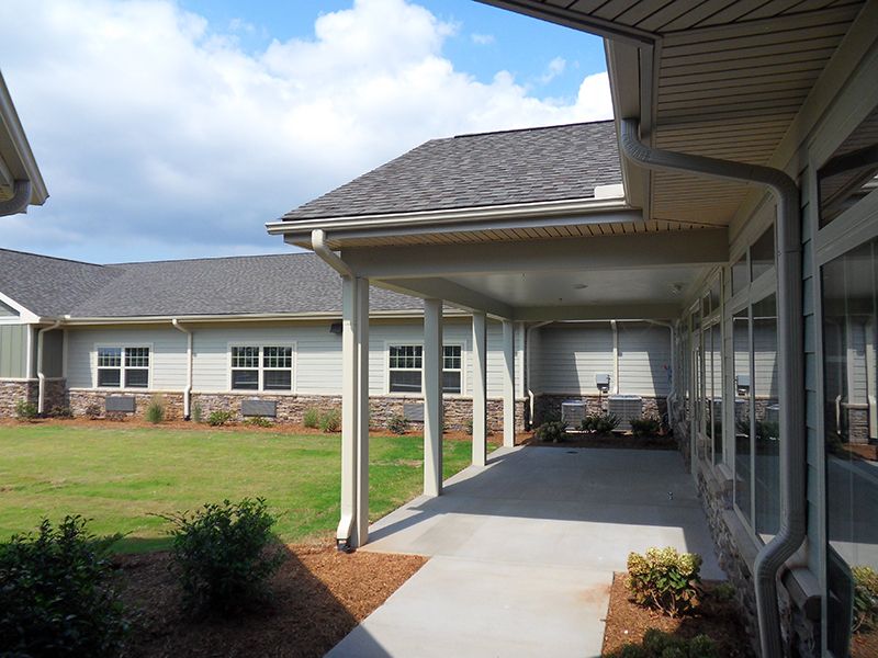 A covered walkway leading to a building surrounded by a well-maintained lawn and garden.