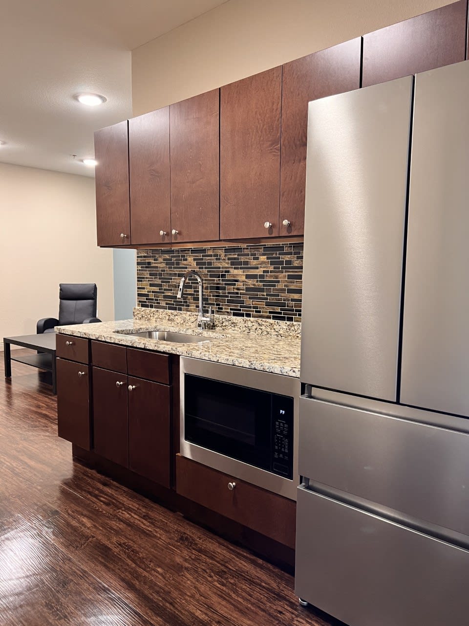 A modern kitchen with wooden cabinets, stainless steel refrigerator, and stone backsplash.