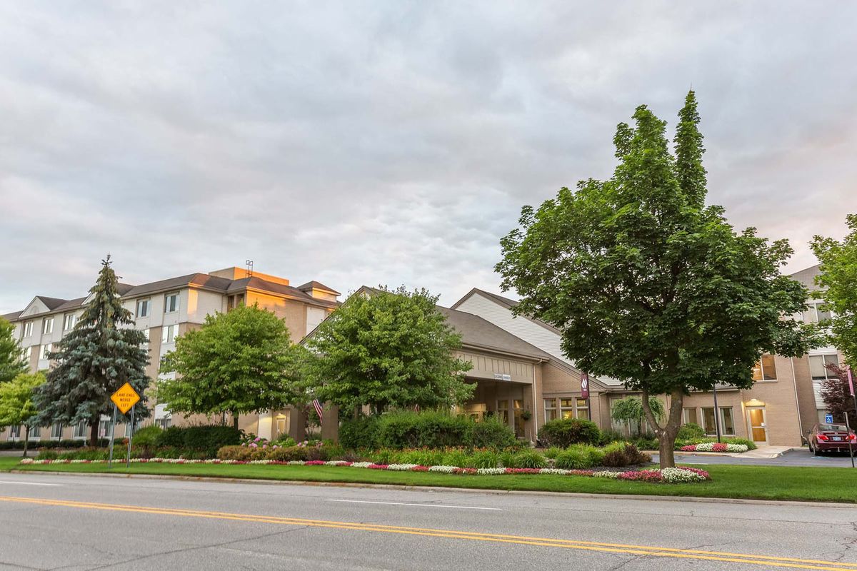 A suburban scene with a building surrounded by trees under a cloudy sky.