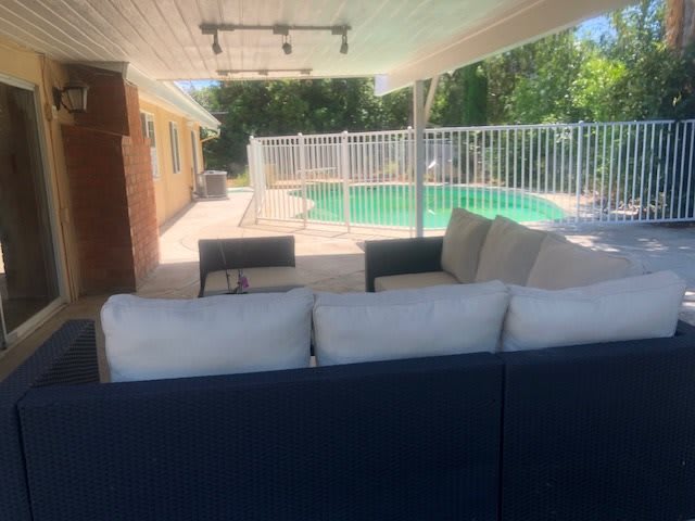A comfortable patio area with a sofa, overlooking a fenced swimming pool in the backyard.