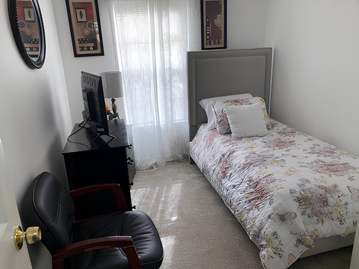 A cozy single bedroom with a floral duvet, featuring a television and an armchair.