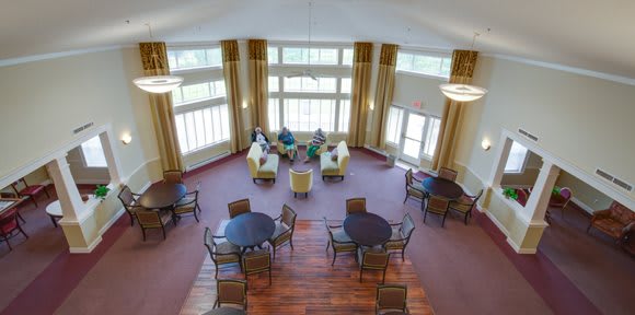 A spacious lounge area with large windows, featuring multiple seating arrangements with tables and chairs.