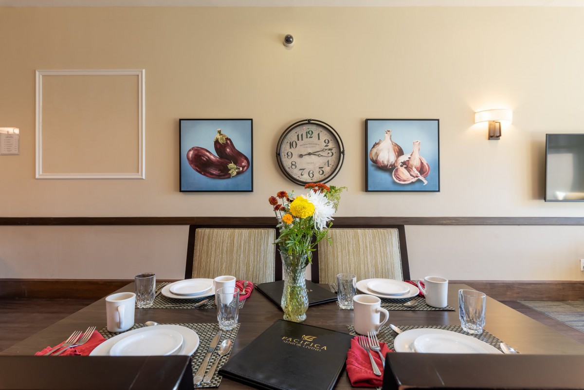 A well-set dining table with a vase of flowers and a wall clock in the background.