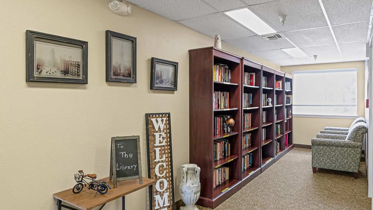 A cozy library interior with bookshelves, decorative items, and a welcome sign.