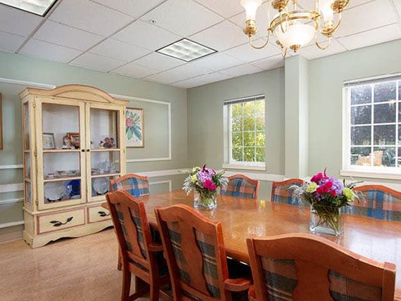 A well-furnished conference room with a long wooden table, surrounded by chairs and adorned with floral arrangements.