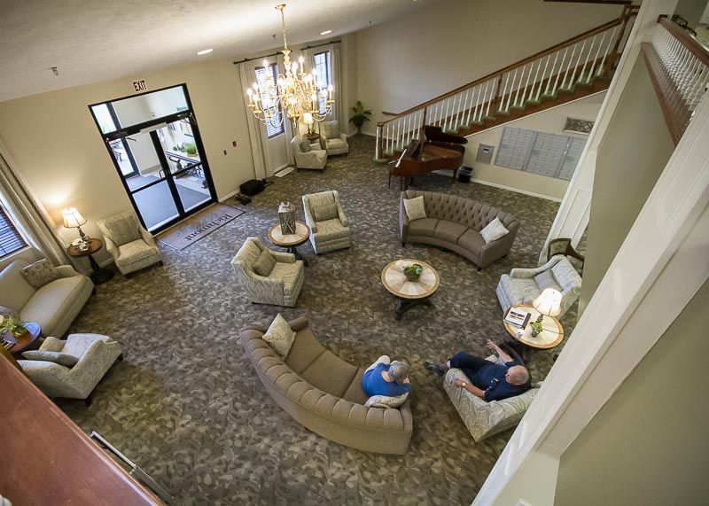 A spacious lobby with a seating area, featuring sofas and armchairs, illuminated by a large chandelier and accompanied by a staircase.