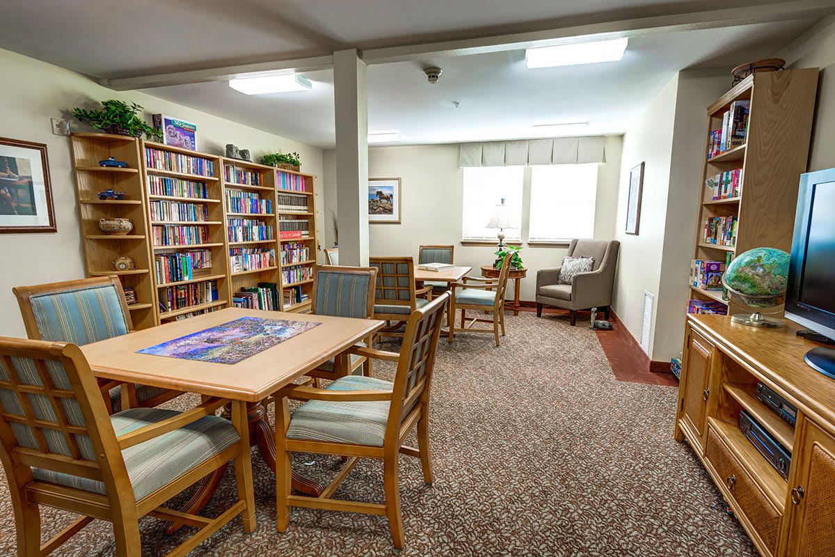 A cozy library area with bookshelves, tables, and chairs for reading.