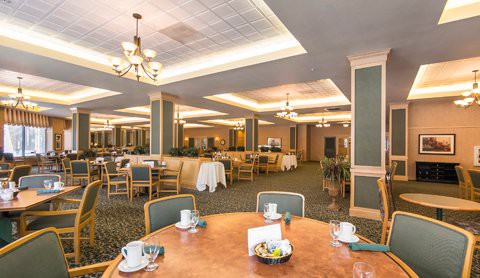 A spacious, elegantly decorated dining room with neatly arranged tables and chairs, adorned with chandeliers.
