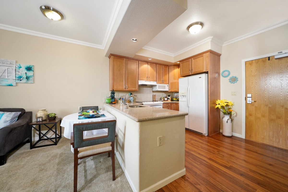 A cozy kitchen and dining area with wooden cabinets, a refrigerator, and a small dining table adorned with flowers.