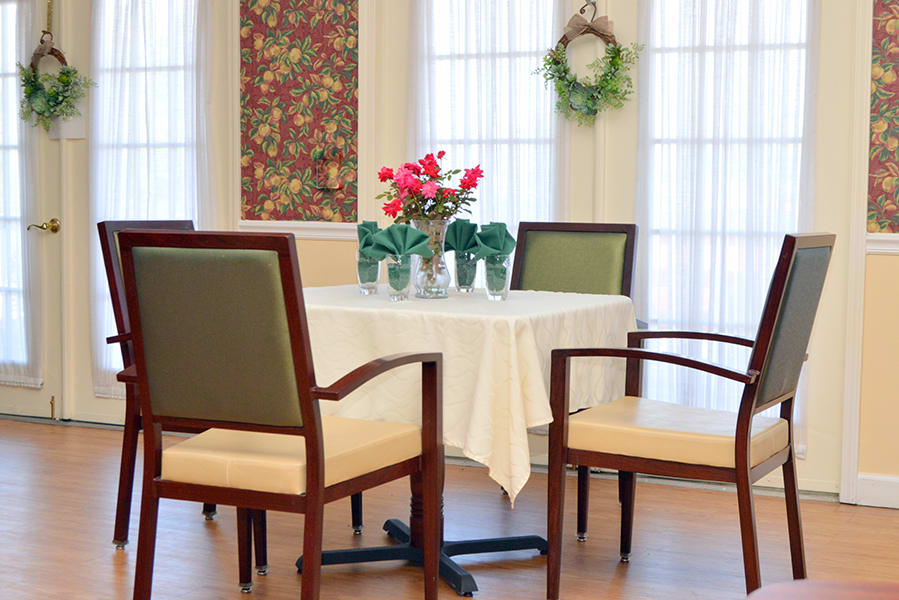 A cozy dining area with a neatly set table, surrounded by chairs and decorated with flowers and a wreath.