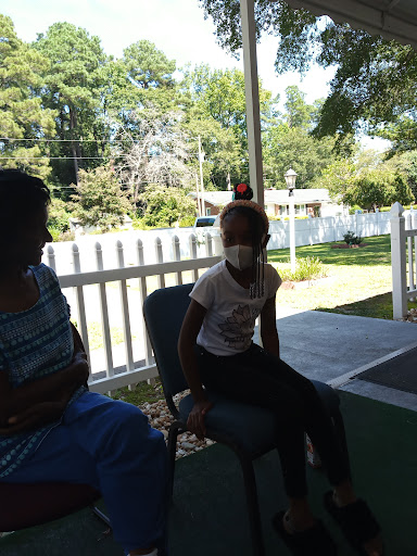 A child wearing a mask sits next to an adult, enjoying a sunny day outdoors.