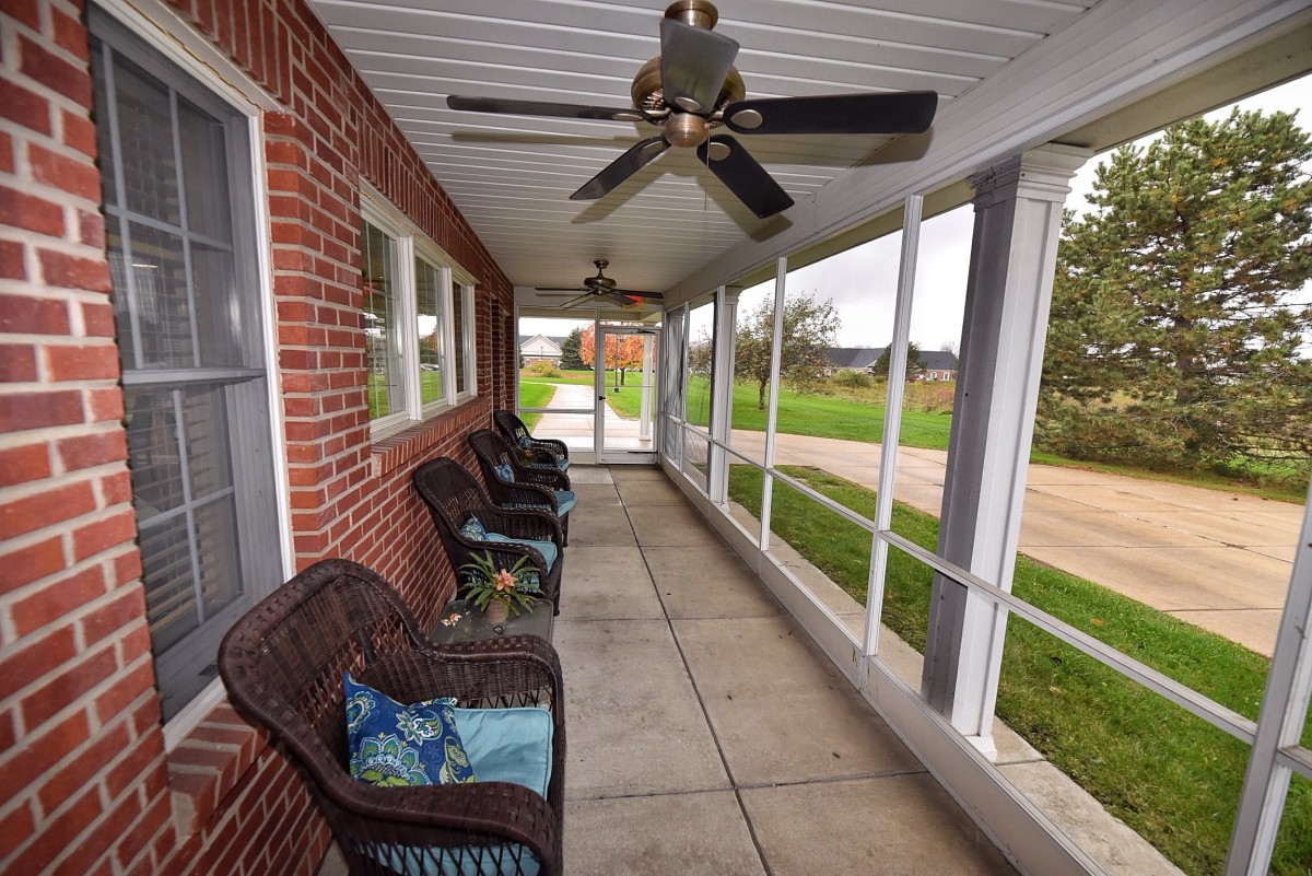 A cozy porch with comfortable seating and a ceiling fan, overlooking a rural setting.