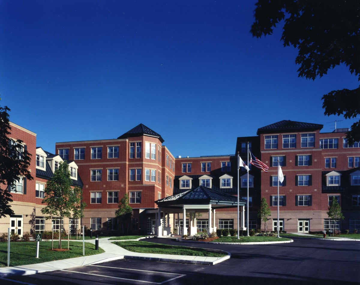 A large brick hospital building with multiple floors and a welcoming entrance under a clear blue sky.