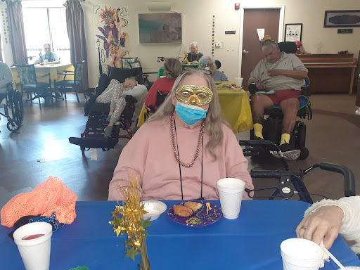 An elderly person enjoying a meal at a community gathering, surrounded by colorful decorations and others in the background.