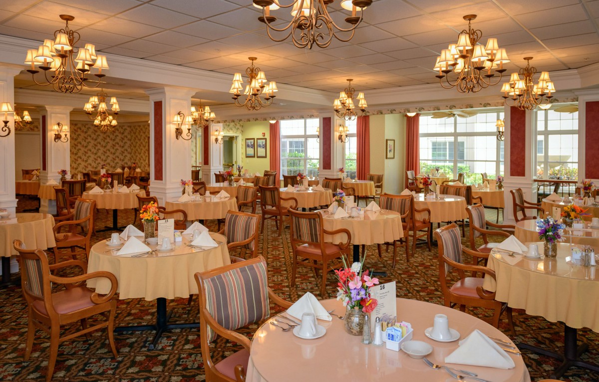 An elegant dining room with round tables set for guests, featuring chandeliers and classic decor.