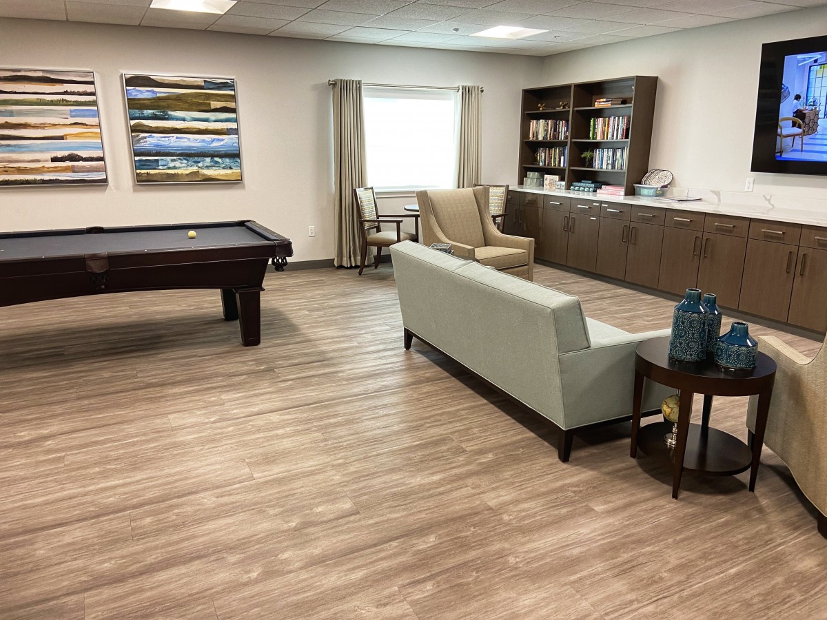 A cozy living space featuring a pool table, comfortable sofa, and bookshelves, with stylish decor and wood flooring.