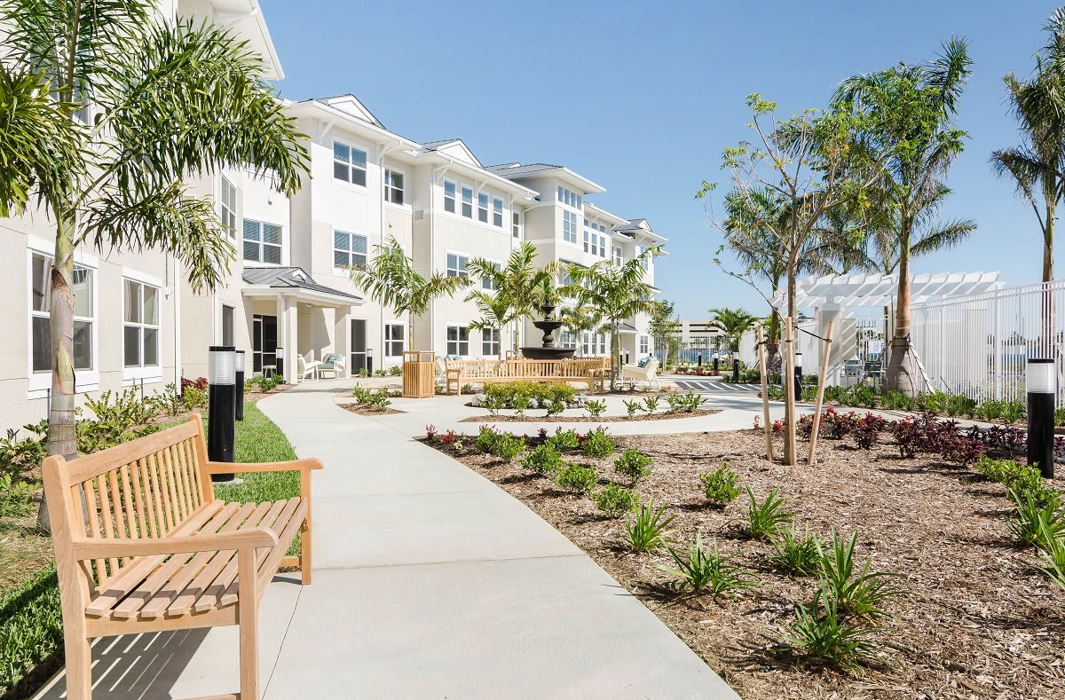 A modern residential building with landscaped pathways and benches surrounded by tropical plants.
