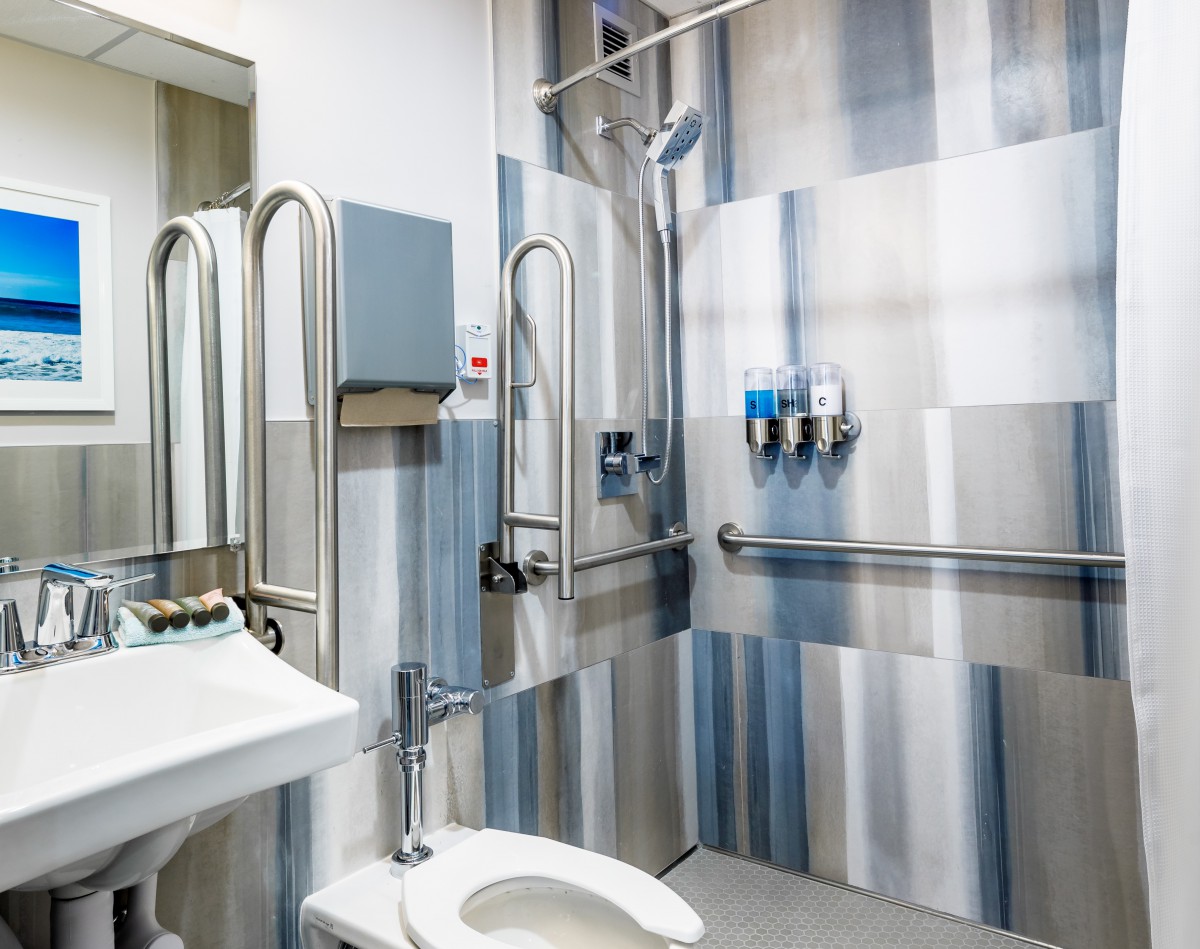 A well-equipped accessible bathroom featuring handrails, a toilet, sink, and shower.